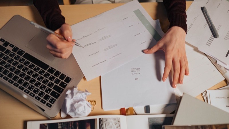 Person arbeitet am Laptop zwischen Unterlagen