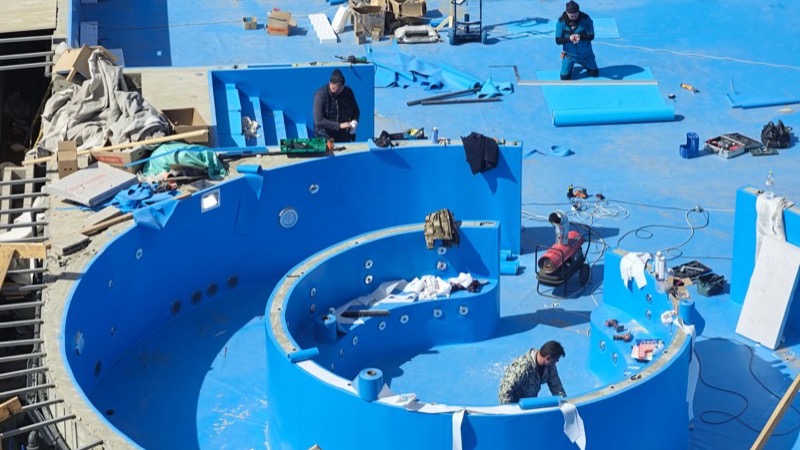 Arbeiter verkleiden ein neu gebautes Schwimmbecken im Garten